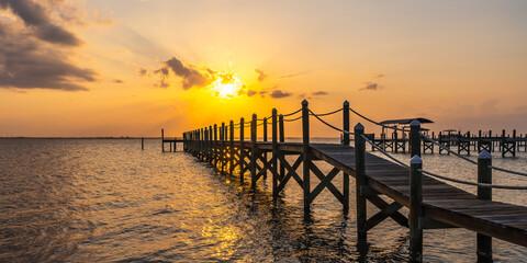 Obraz premium Wooden pier on poles with rope railings during a yellow sunset over the Indian River, Vero Beach, Florida