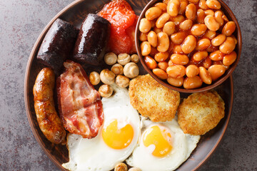 Full fry up English breakfast with fried eggs, sausages, bacon, black pudding, beans, tomato closeup in the plate on the table. Horizontal top view from above - obrazy, fototapety, plakaty