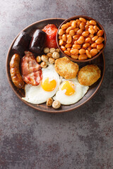 Irish breakfast with fried egg, sausages, black pudding, baked beans, bacon, tomato, hash browns and grilled mushrooms closeup in the plate on the table. Vertical top view from above