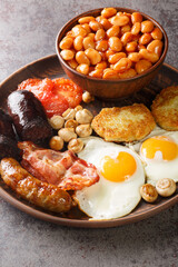 Irish breakfast with fried egg, sausages, black pudding, baked beans, bacon, tomato, hash browns and grilled mushrooms closeup in the plate on the table. Vertical