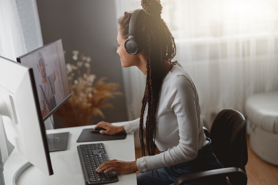Young happy mixed-race woman speaking on video call on computer wearing headphones