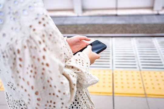 電車のホームでスマートフォンを使う女性
