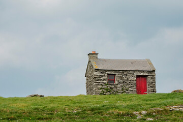 Small traditional stone shed or storage on a hill and a green field. Blue cloudy sky in the background. Nature scene. Inisheer, Aran island, Ireland. Irish nature landscape.