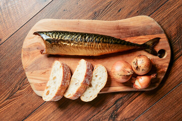 Smoked mackerel and onion and fresh bread on a wooden board and table. Taste of Poland. Fish industry product.