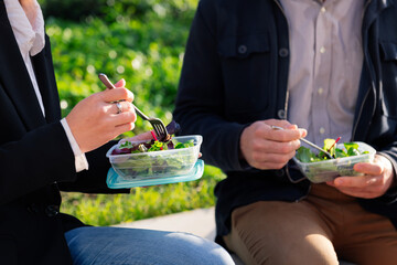 detail of the hands of two people eating a salad in a park during a work break, concept of healthy...