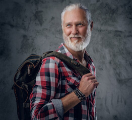 Shot of stylish old man dressed in plaid shirt carrying backpack against dark background.