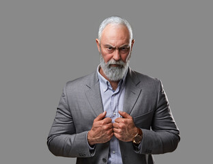 Shot of stylish elderly man with beard staring at camera against grey background. - obrazy, fototapety, plakaty