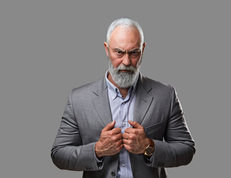 Shot of stylish elderly man with beard staring at camera against grey background.