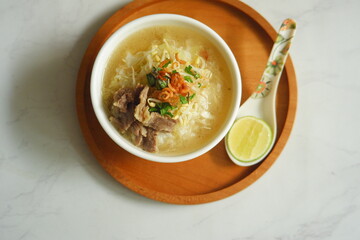 a bowl of beef vegetables clear soup served with rice named soto in Bahasa