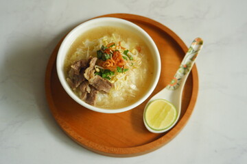 a bowl of beef vegetables clear soup served with rice named soto in Bahasa