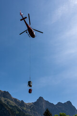 Fototapeta na wymiar helicopter carrying a bucket of cement to a distant mountain hut in the Swiss Alps