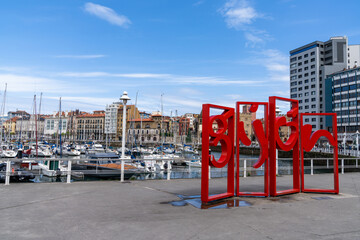 view of the sports marina and harbor in Gijon with the town name in red letters