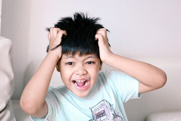A Little Asian boy itchy his hair.