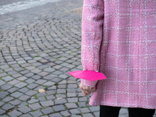 View from Behind of a Lady in a Pink Jacket with a Pink Protective Mask stuffed in her Arm Walking down the Street