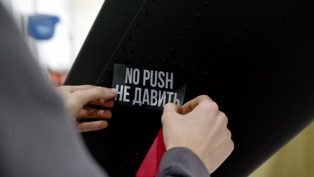 worker sticks sticker on black surface with the inscription NO PUSH. white inscription on transparent background decal is pasted on wing of helicopter or aircraft in hangar on vehicle upgrade.
