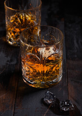 Single malt scotch whiskey in crystal glasses with ice cubes on wooden background
