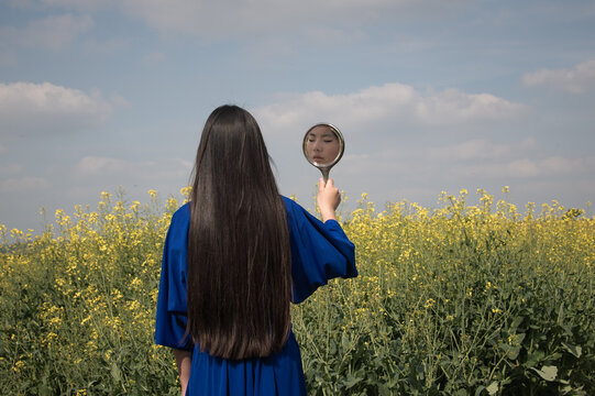 fine art portrait of woman in a field of yellow flowers holding hand mirror