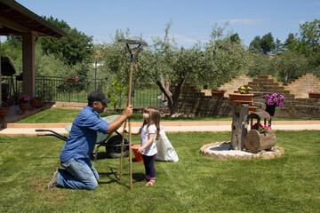Picture of a gardener dad with his daughter in the backyard while they aerate and collect the...