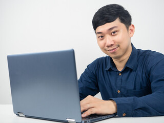 Male employee using laptop for work and looking at camera and smiling