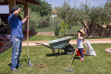 Photo of a gardener father and daughter wiping sweat from their foreheads as they rake and aerate...