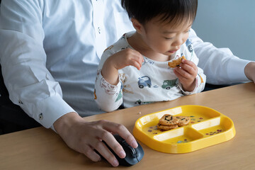 お菓子を食べる子供とリモートワークするお父さん