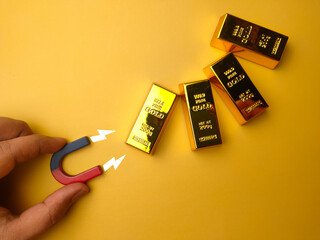 Hand holding magnet attract the gold bar on a yellow background.