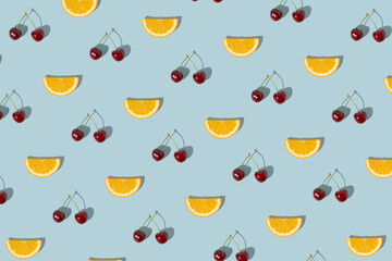 Cherries and orange slice on blue background. Summer fruit background pattern.