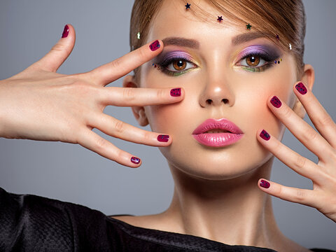 Portrait of a beautiful woman with bright makeup. Closeup female face with purple eye make-up. Pretty, sexy girl with violet nails near face. Stylish fashion model with a short slick hair