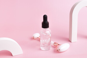 Glass bottle with oil, roller for face massage on a pink background with arch. Cosmetic facial skin care and spa. Natural treatment concept.
