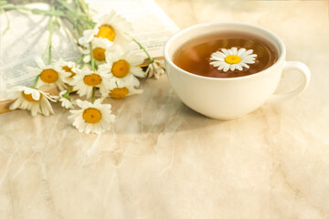 a cup of herbal tea, chamomile and a book on the table. Summer breakfast
