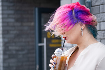 Close-up portrait of curly Caucasian woman with multi-colored hair wearing glasses. The hairstyle model is drinking a cold drink