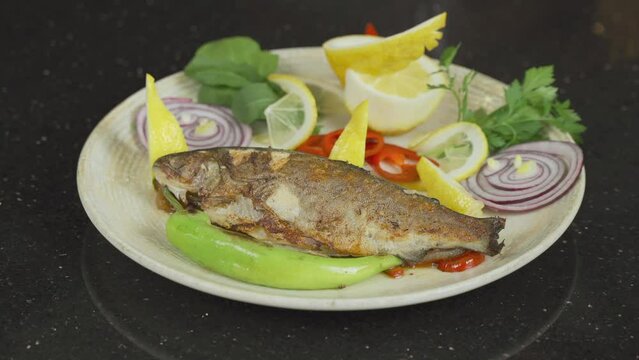 Fish serving platter.
Fish serving platter is placed on the table. The chef puts lemon slices on the fish among the green vegetables.
