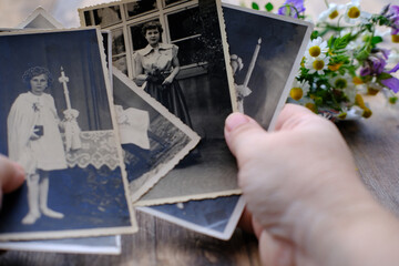 close-up of female hand hold old family photos, vintage photographs of 50s, 40s, black retro accordion camera on wooden table, concept of genealogy, memory of ancestors, family tree, home archive