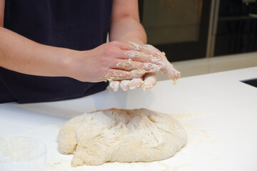 Home cooking. A young woman works with yeast dough in a modern kitchen. A young woman is kneading a dough, engaged in cooking homemade bakery.