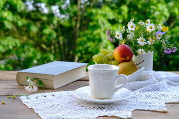 tea, coffee in white mug on saucer, book, fruits, lace napkin, bouquet of wild flowers on wooden...