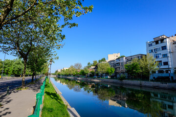 Landscape with large green old trees near Dambovita river and clear blue sky in the center of Bucharest, Romania, in a sunny spring day.