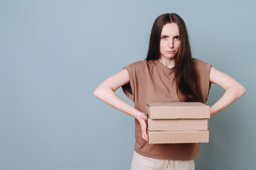 Young pretty beautiful serious woman holding a stack of cardboard boxes in front of her and looking at the camera