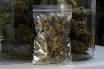 Dry and trimmed cannabis buds stored in a plastic bag on glass jars background with buds. Medical...