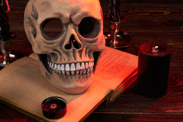 Wicca satanic ritual concept. Humans skull on the satanic bible book. Extinguished candels indoors....
