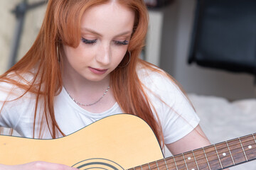 young woman playing acoustic guitar at home, portrait close-up