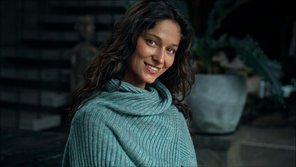 cute European brunette in denim jacket dress and blue scarf sits and poses for camera inside building