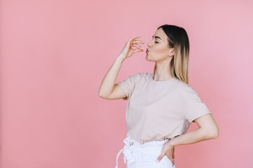 A girl on a soft pink background with her hands and face shows that she is tasting delicious food with her eyes closed