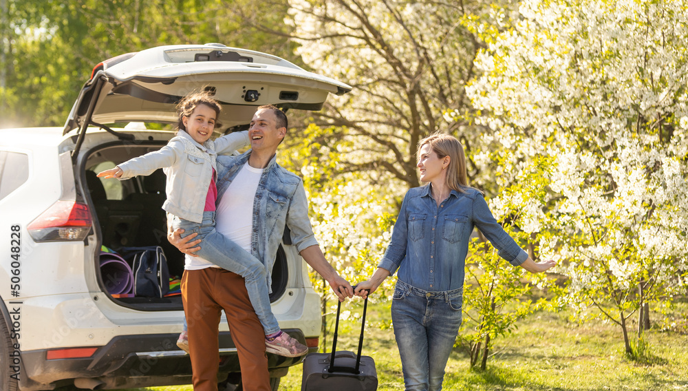 Canvas Prints Happy family standing together near a car with open trunk enjoying view of rural landscape nature. Parents and their kid leaning on vehicle luggage compartment. Weekend travel and holidays concept.