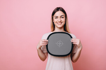 Smiling girl holding a gray card in her hands for white balance on a pink background