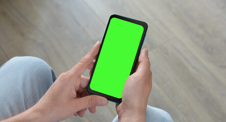 A man holds a smartphone with a green screen.Mockup. Copy space for text