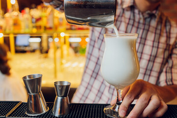 Close up shot of bartender hand pouring Cream mocktail in a glass from shaker.