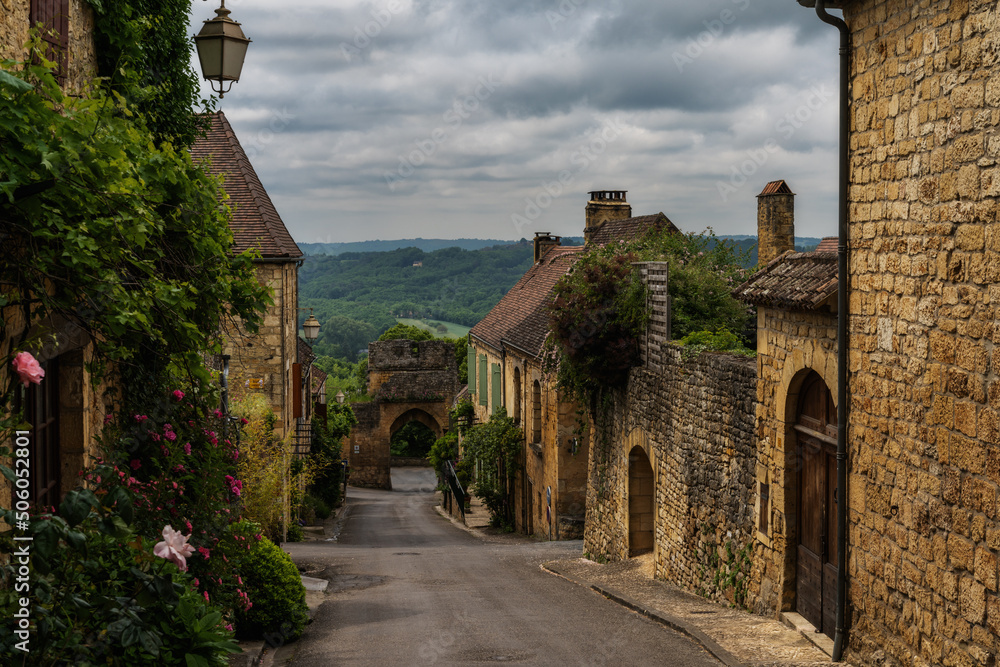 Wall mural picturesque street with stone houses and blossoming flowers in the historic village of Domme in the Dordogne Valley