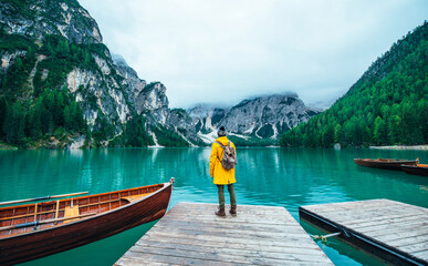 Mountain stories. Happy backpacker on a wanderlust vacation. Man with a yellow raincoat standing in front the lake and enjoying the view - obrazy, fototapety, plakaty