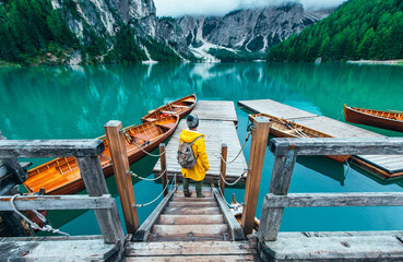 Mountain stories. Happy backpacker on a wanderlust vacation. Man with a yellow raincoat standing in front the lake and enjoying the view - obrazy, fototapety, plakaty