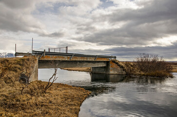Simple concrete bridge across a stream coming from the mountains and flowing towards lake Myvatn in Iceland
